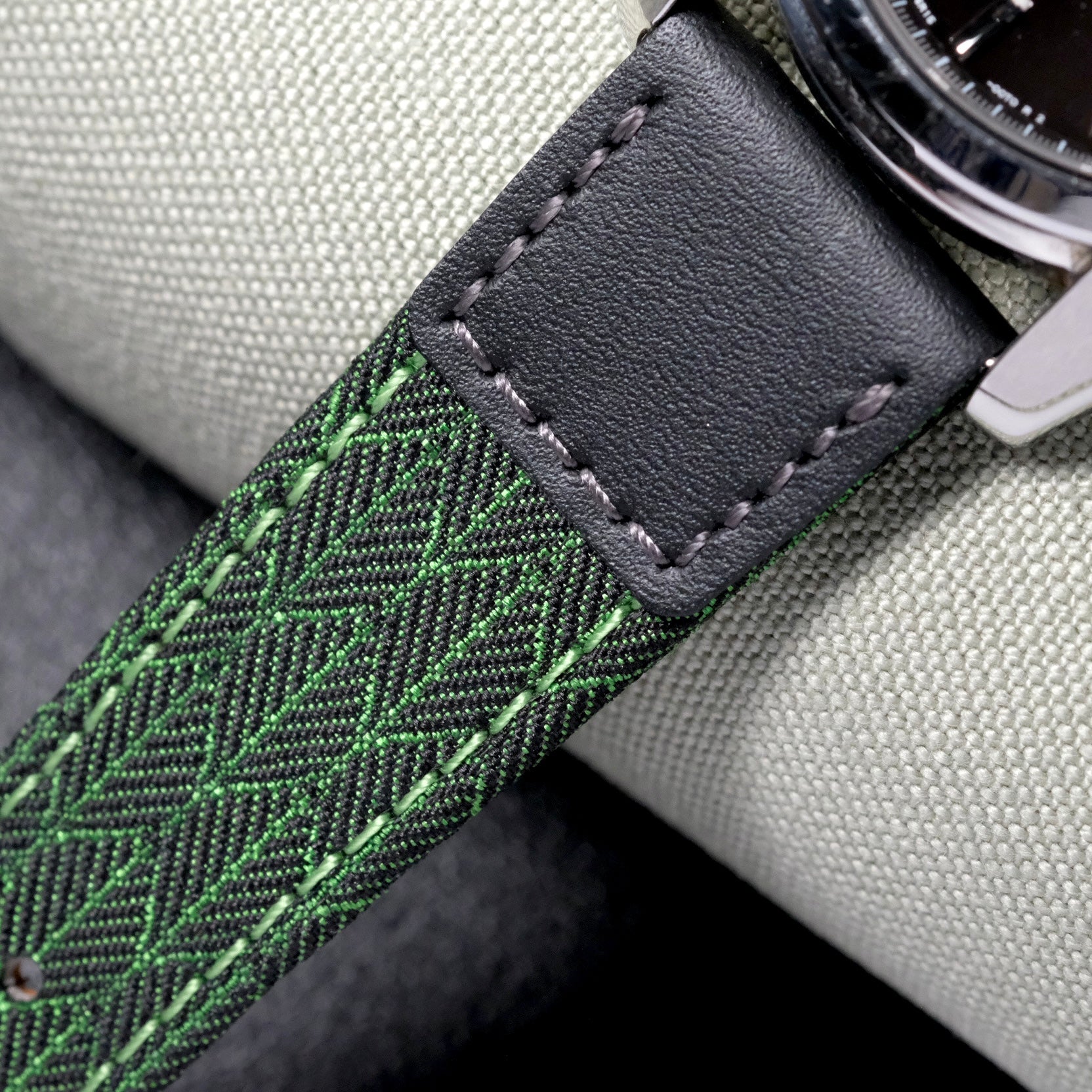 Close-up of the RSM Watch Straps Art Deco Silk Watch Strap in Green, featuring black leather and green patterned fabric with detailed stitching, resting on a light gray textured surface.