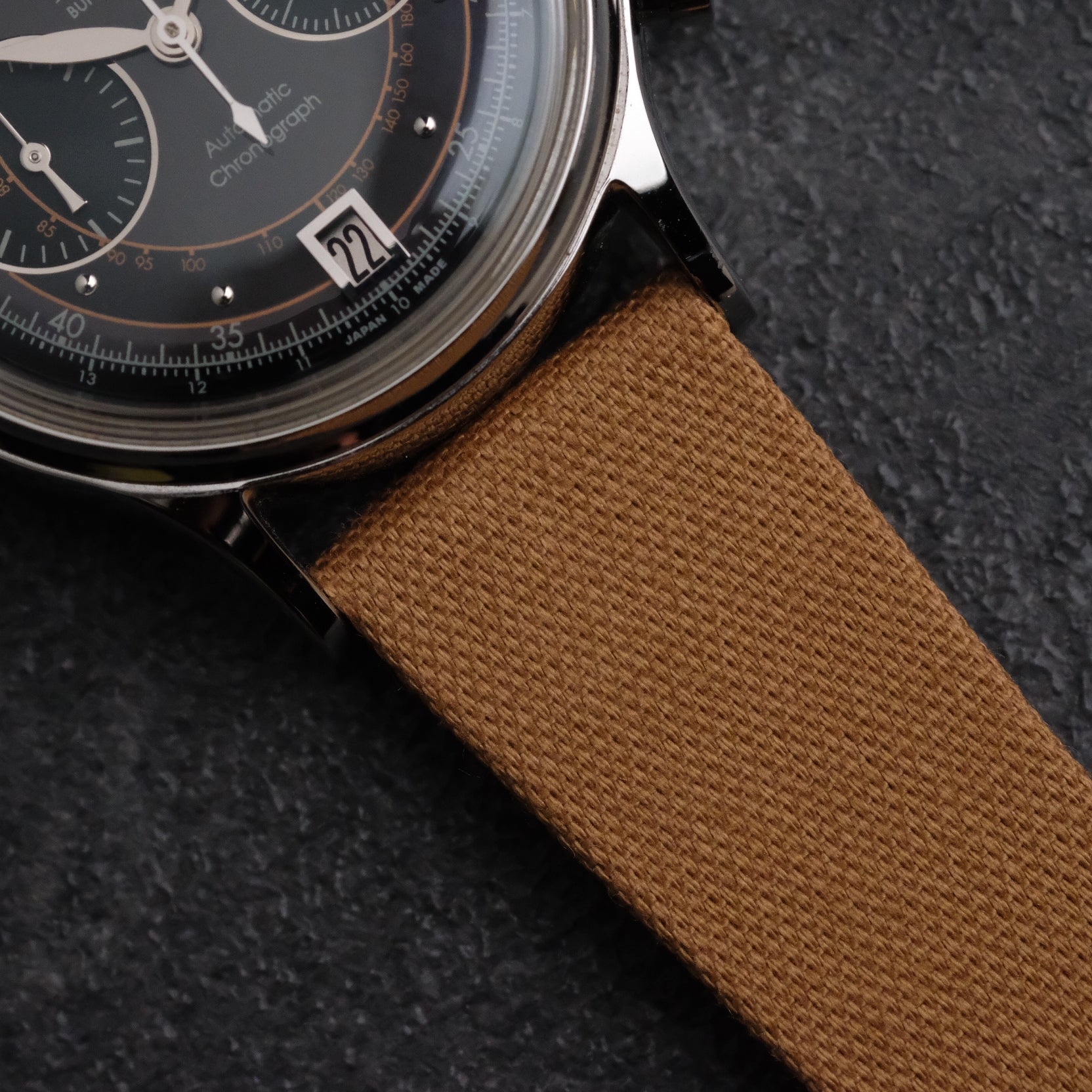 Light brown tea-colored woven Japanese canvas strap on a Chrono 2 Kurono Tokyo watch with a polished steel case and lacquered black dial.