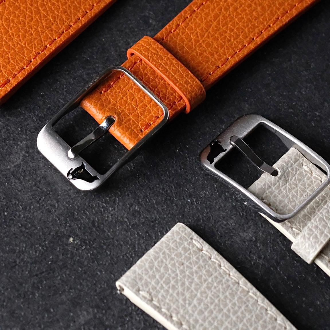 Close up of the silver buckle with walrus logo and Italian epsom leather watch straps in orange and white.