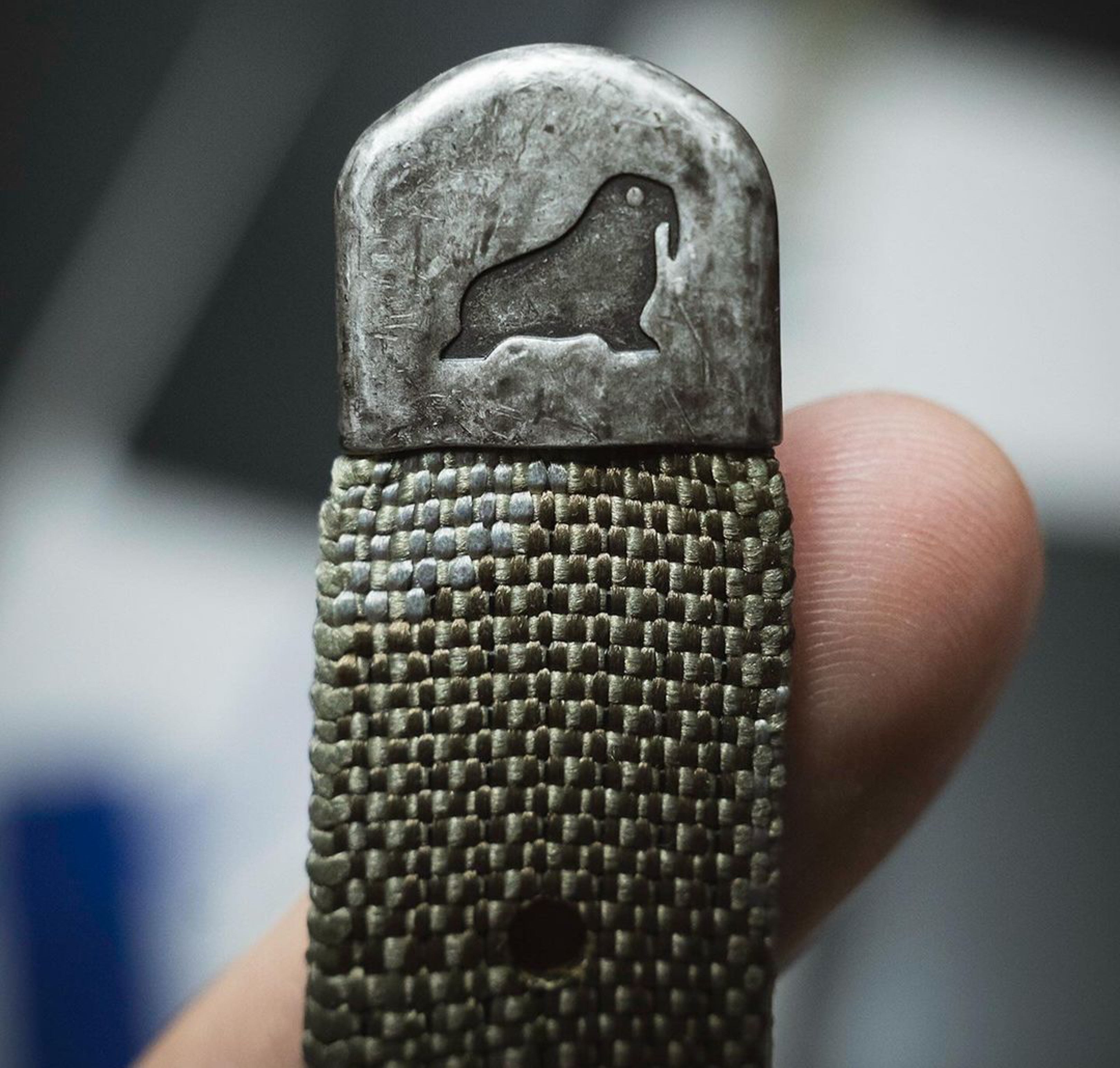 Camo woven strap with distressed tip and stamped walrus logo, featuring pre-dyed IRR camo tones blending seamlessly with forest surroundings.