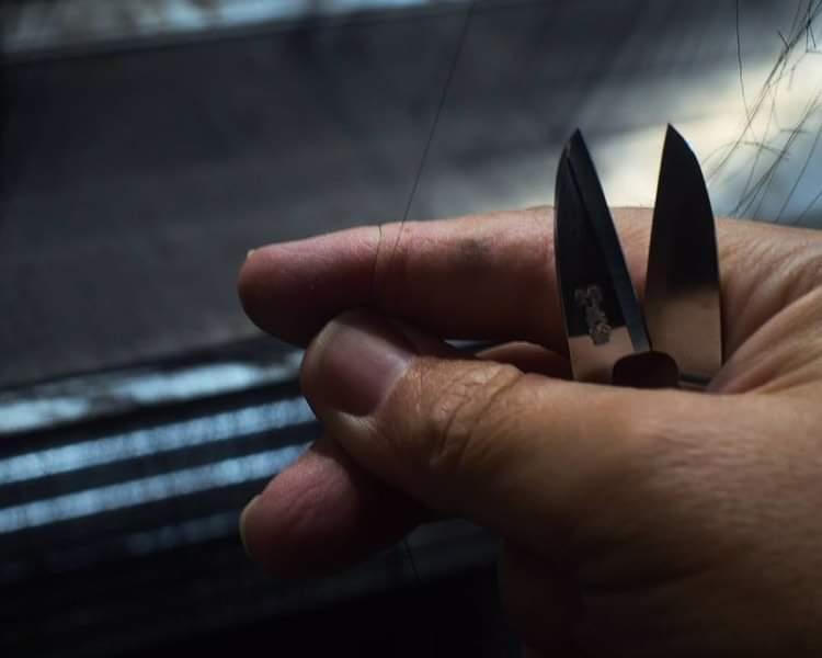 Close-up of working hands threading silk with small scissors, showcasing delicate craftsmanship in the process.