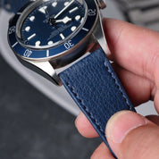 A hand holds a Tudor watch with a blue dial, white markers, rotating bezel, and an RSM Watch Straps Italian Epsom Leather Watch Strap in Navy Blue.