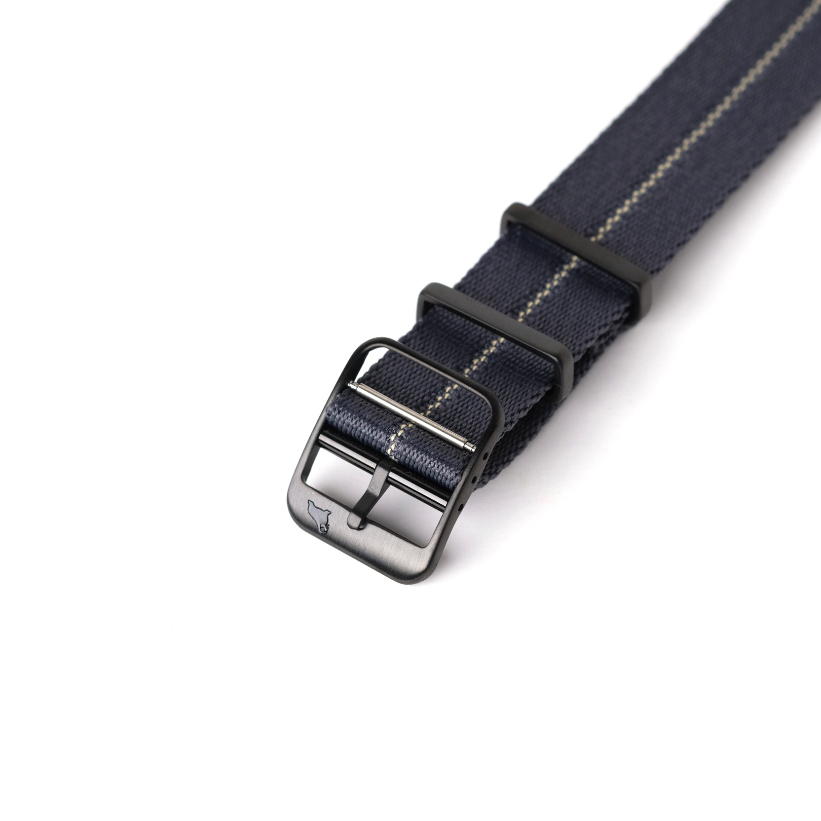 A close-up of the RSM Watch Strap Engraved Stripe in Blue Grey Patina features a dark blue jacquard weave strap, light stitching, and a black metal buckle.