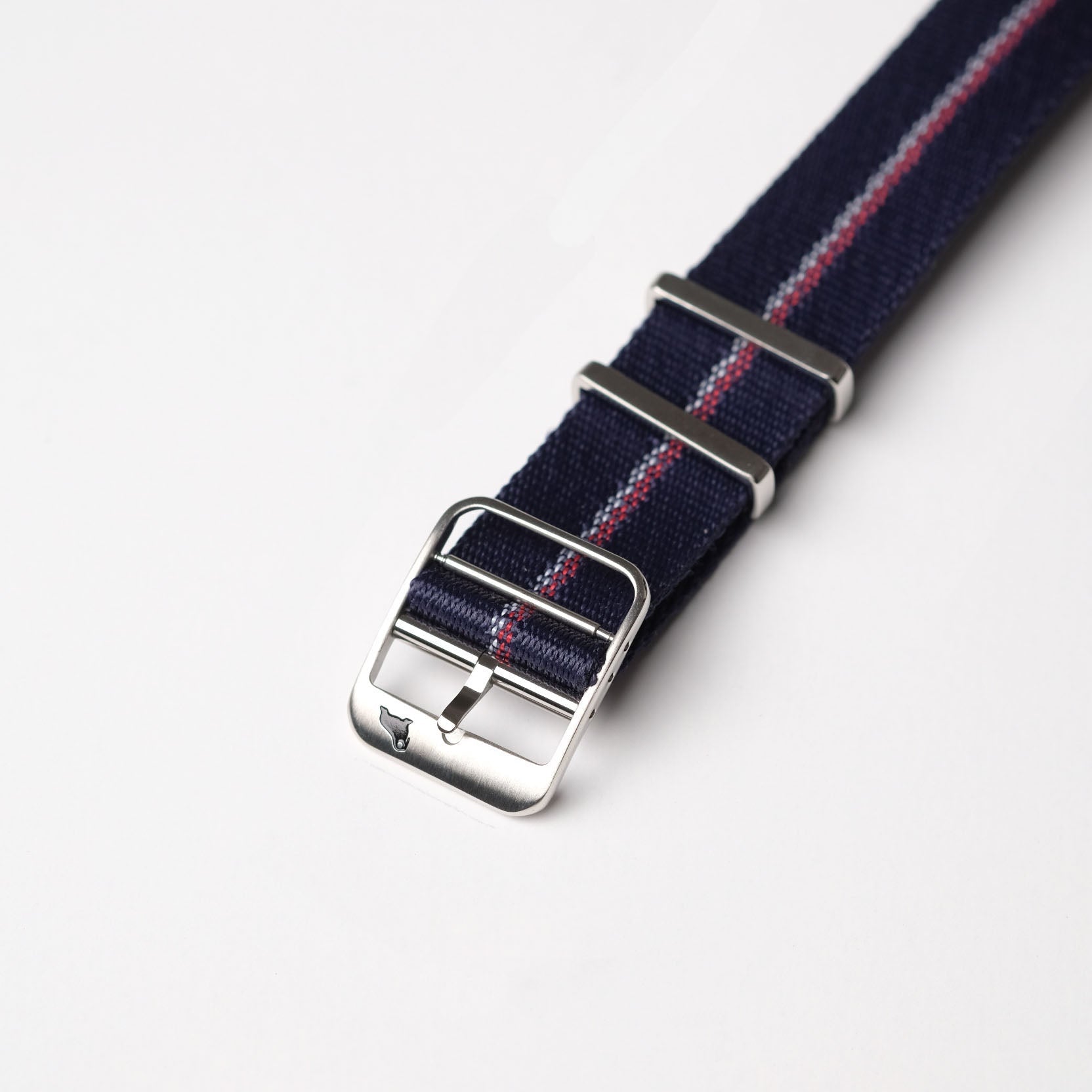 A close-up of the RSM Watch Strap Engraved Stripe in Red, White, and Blue, featuring a navy blue nylon strap with red and white stripes, silver buckle.
