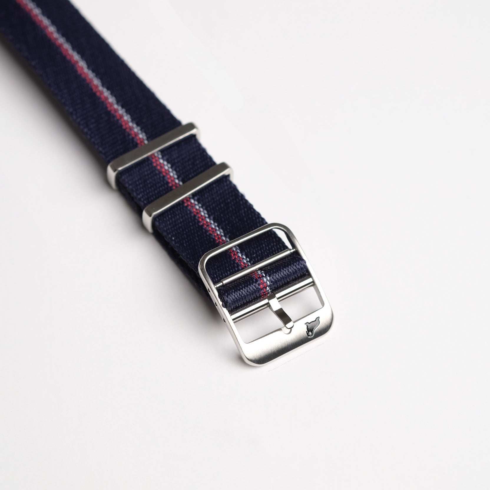 The Engraved Stripe in Red, White, and Blue by RSM Watch Strap features a navy nylon strap with a red and white stripe, silver buckle on a white surface.