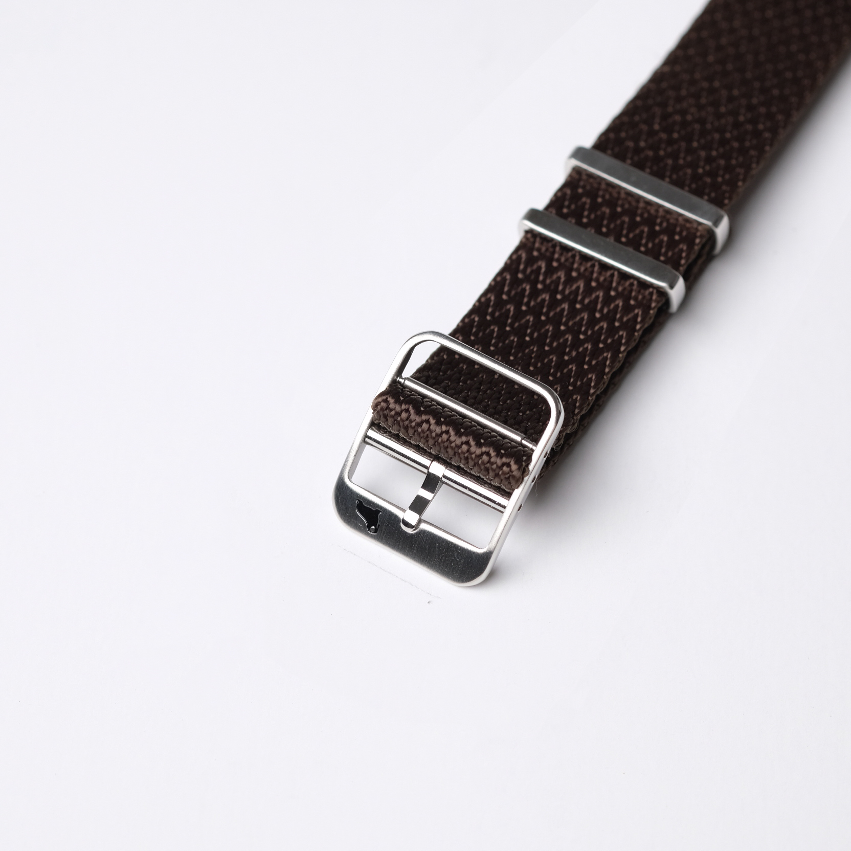 A close-up of the RSM Herringbone Twill in Tobacco Brown watch strap with a silver buckle, set against a white background.