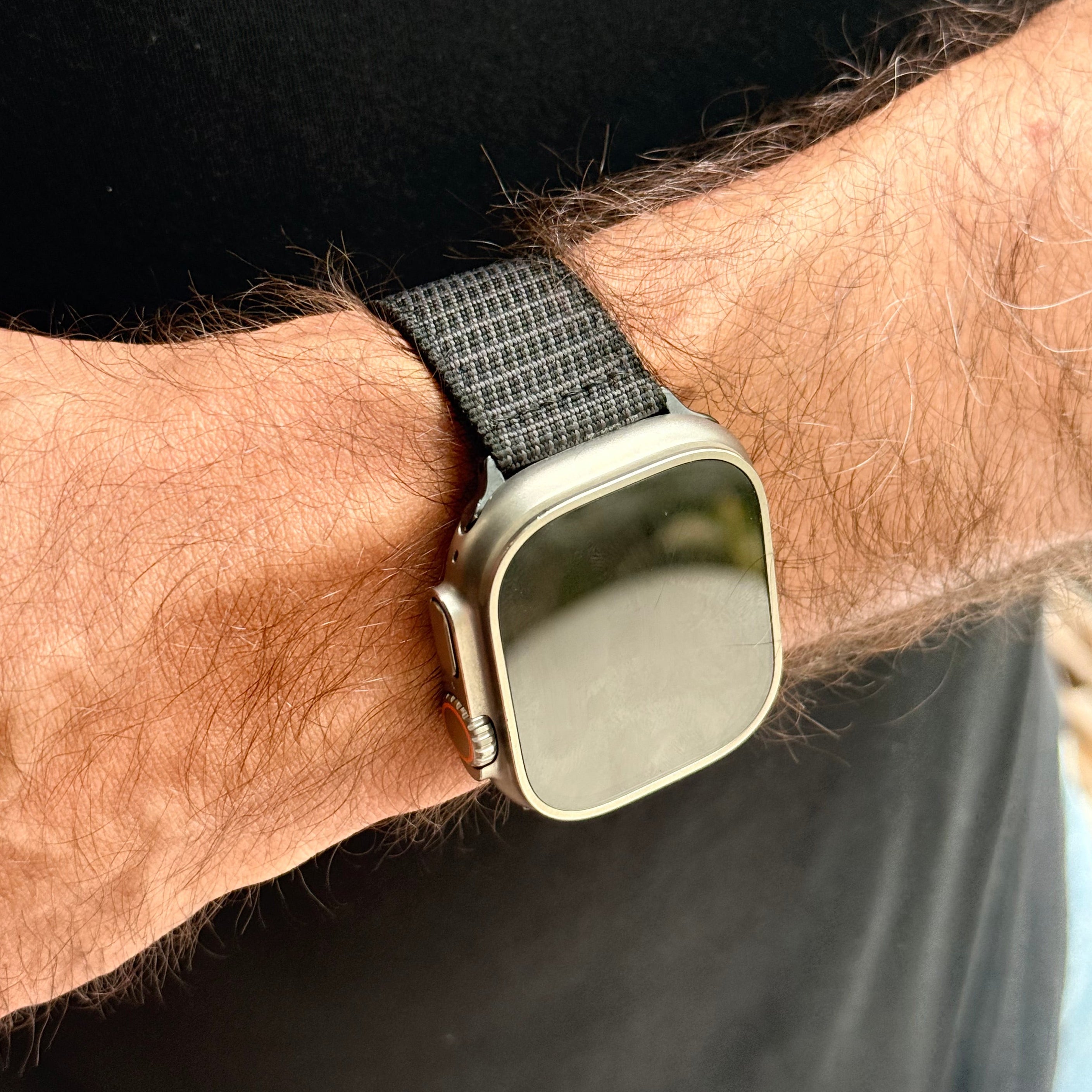 A close-up of a wrist wearing the RSM Watch Strap X-Hatch 2-Piece Watch Strap in Black with a silver-case apple watch, set against a black shirt background.