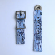 The RSM Watch Strap Ocean Camo 2-Piece Watch Strap features a blue and gray ocean camo pattern, a metal buckle on one piece, and a metal-tipped end with a horse engraving, shown against a light background.