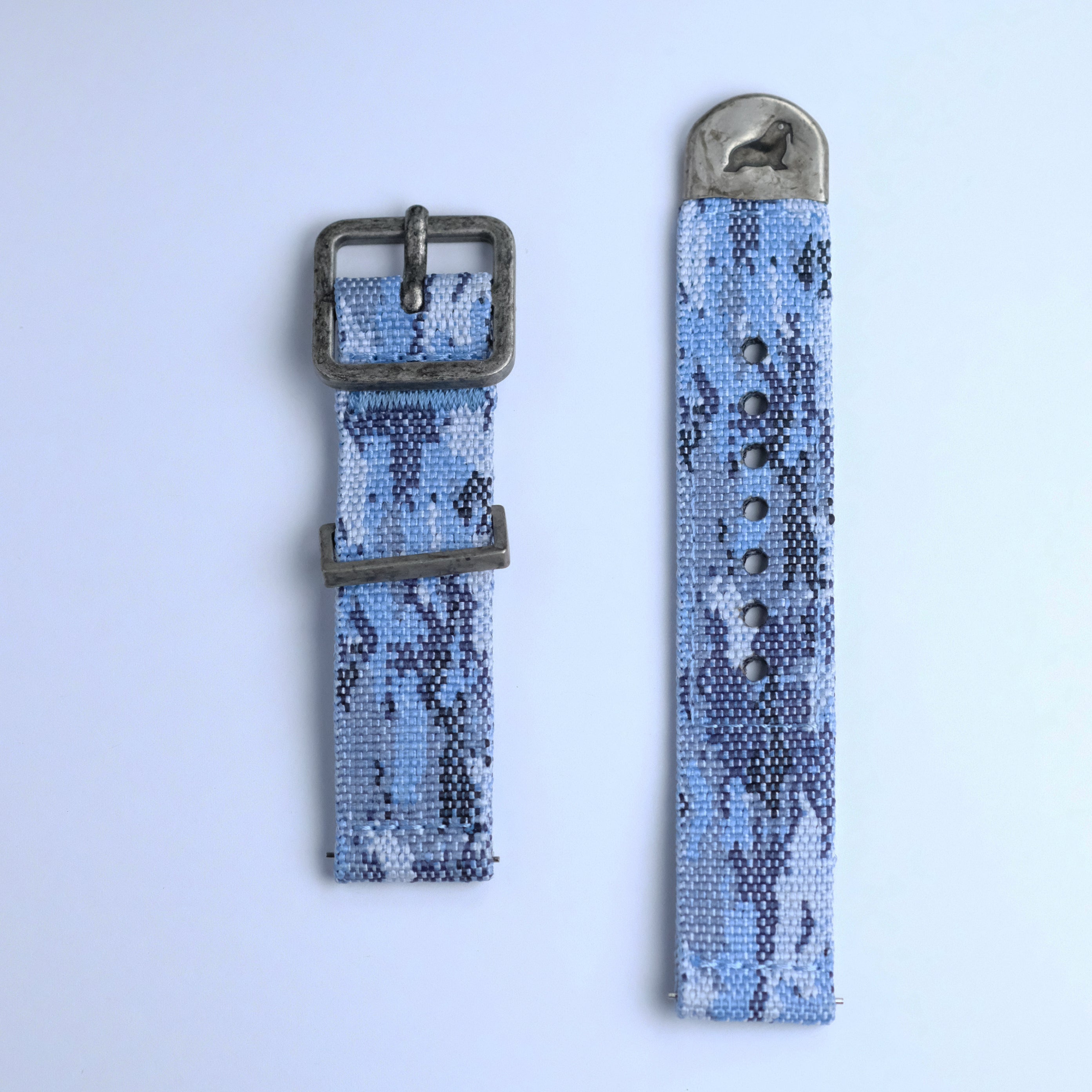 The RSM Watch Strap Ocean Camo 2-Piece Watch Strap features a blue and gray ocean camo pattern, a metal buckle on one piece, and a metal-tipped end with a horse engraving, shown against a light background.
