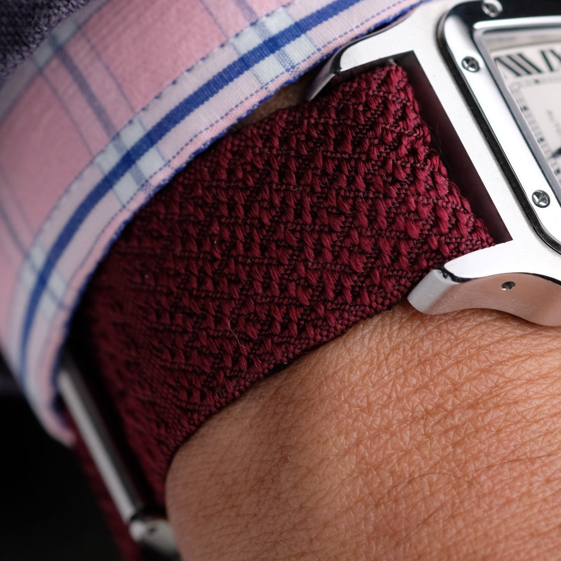 Burgundy high-density luxury silk watch strap in a geometric pattern, worn with a dress watch on a wrist with a checkered sleeve. RSM reversible silk strap.