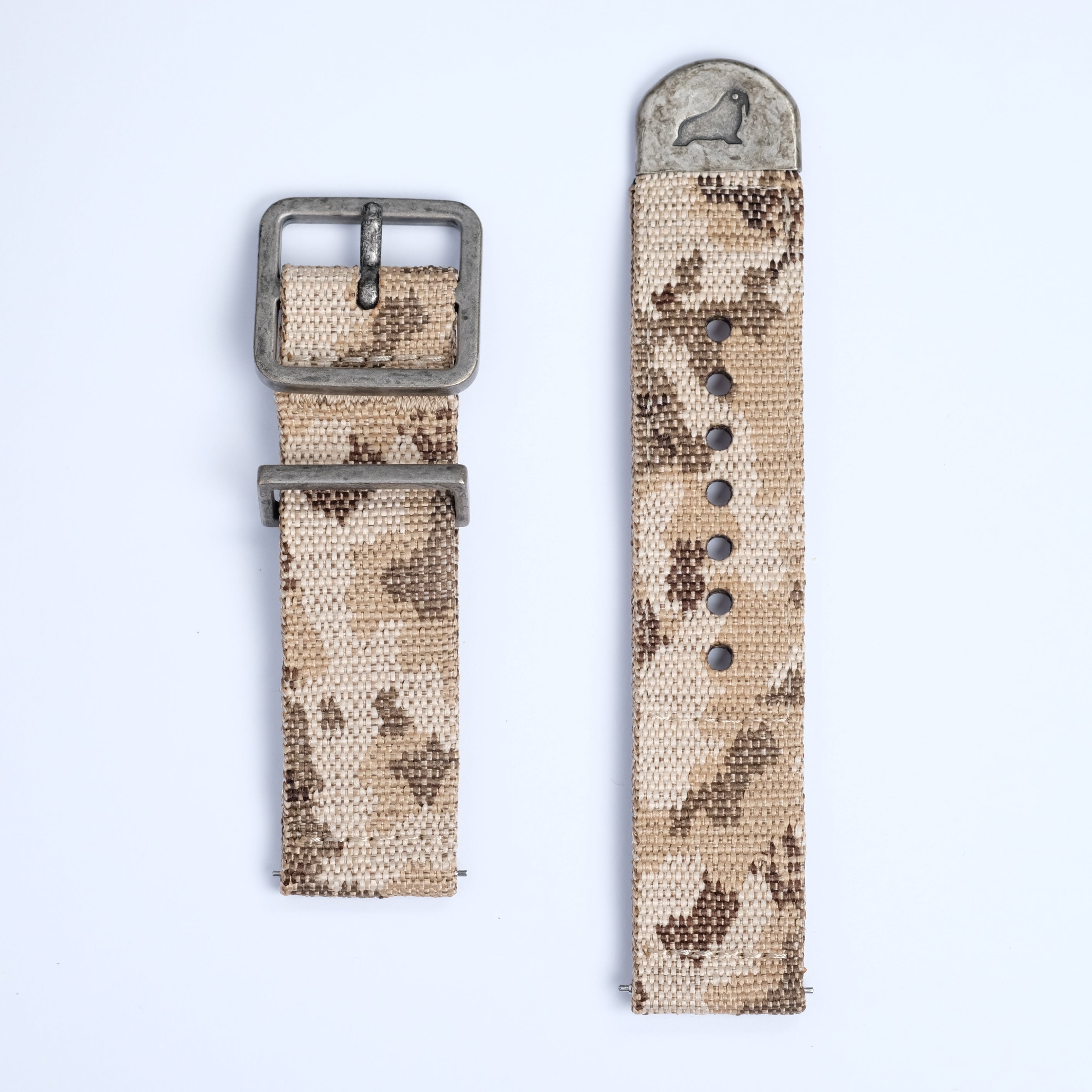 The RSM Watch Strap Desert Camo 2-Piece Watch Strap features desert camouflage-patterned fabric, a metal buckle with a small bird engraving, and multiple holes, all displayed flat on a white background.