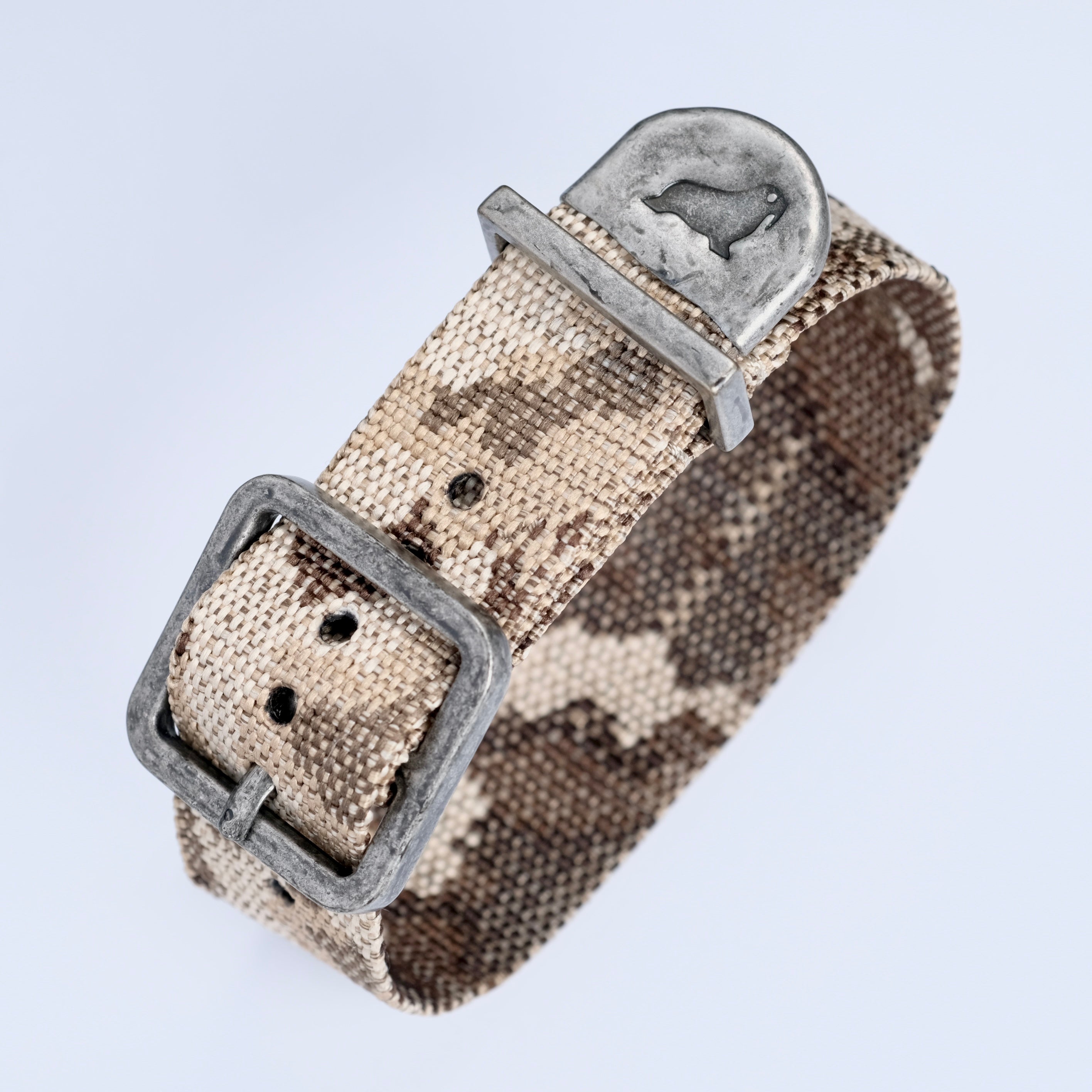 The RSM Watch Strap Desert Camo Zulu Watch Strap features a beige and brown camo fabric, a metal buckle, and a metal loop engraved with a bear silhouette.