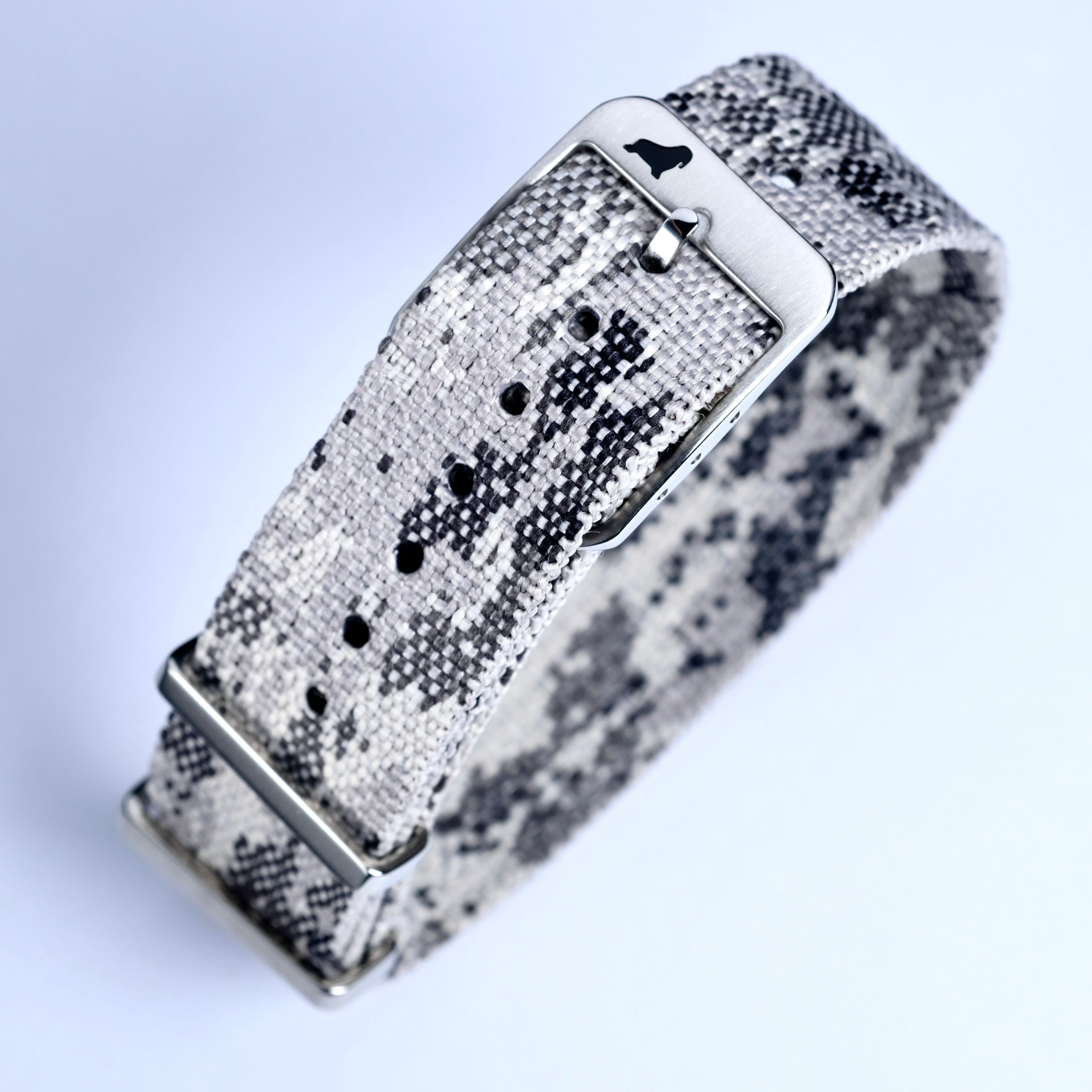 The RSM Watch Strap Snow Camo Adjustable Single Pass features a jacquard woven gray and black camouflage pattern, a silver buckle with a dog silhouette logo, shown close-up against a white background.
