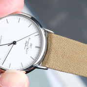Hand holding a watch with a Fine Canvas watch strap by RSM watch strap. against a blurred background