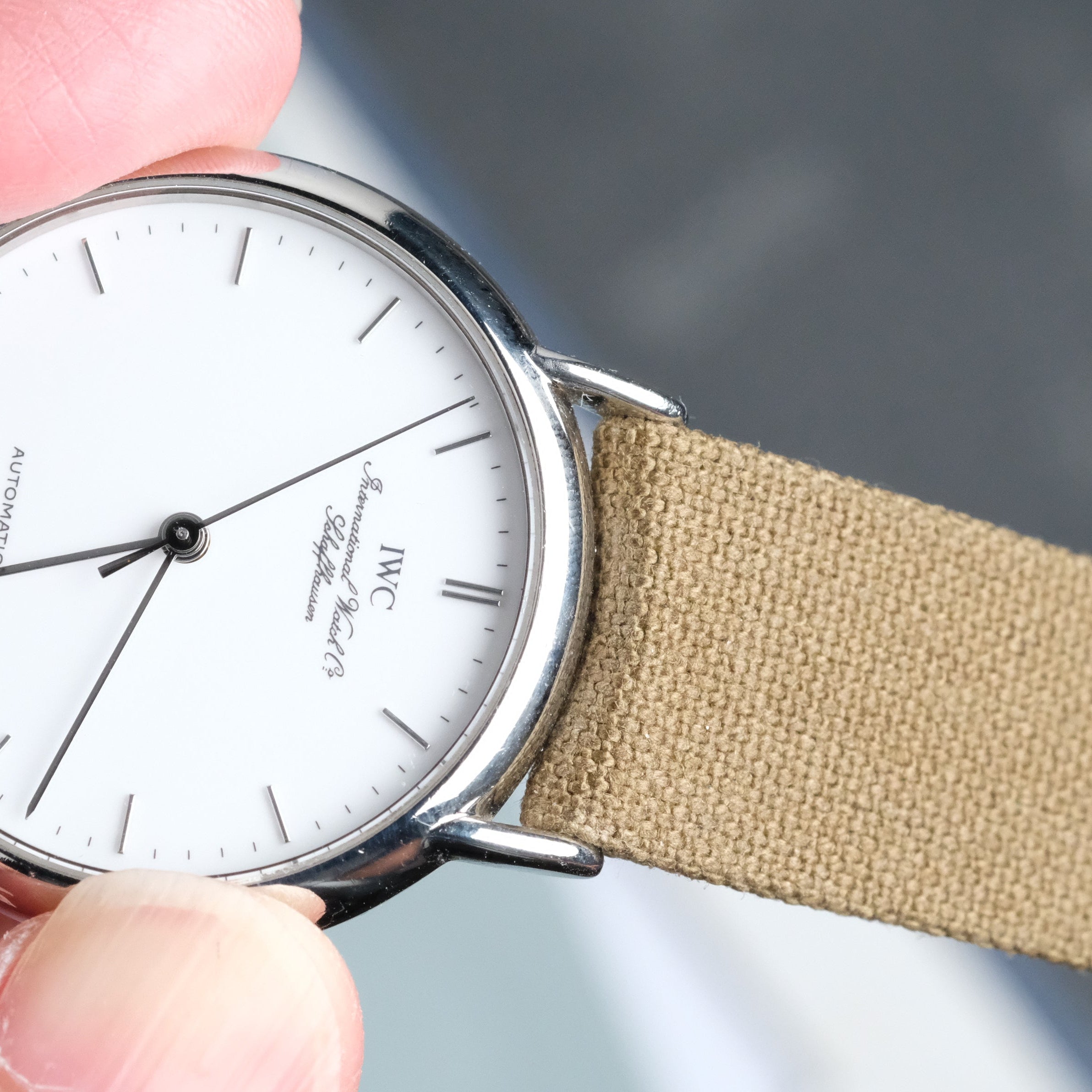 Hand holding a watch with a Fine Canvas watch strap by RSM watch strap. against a blurred background