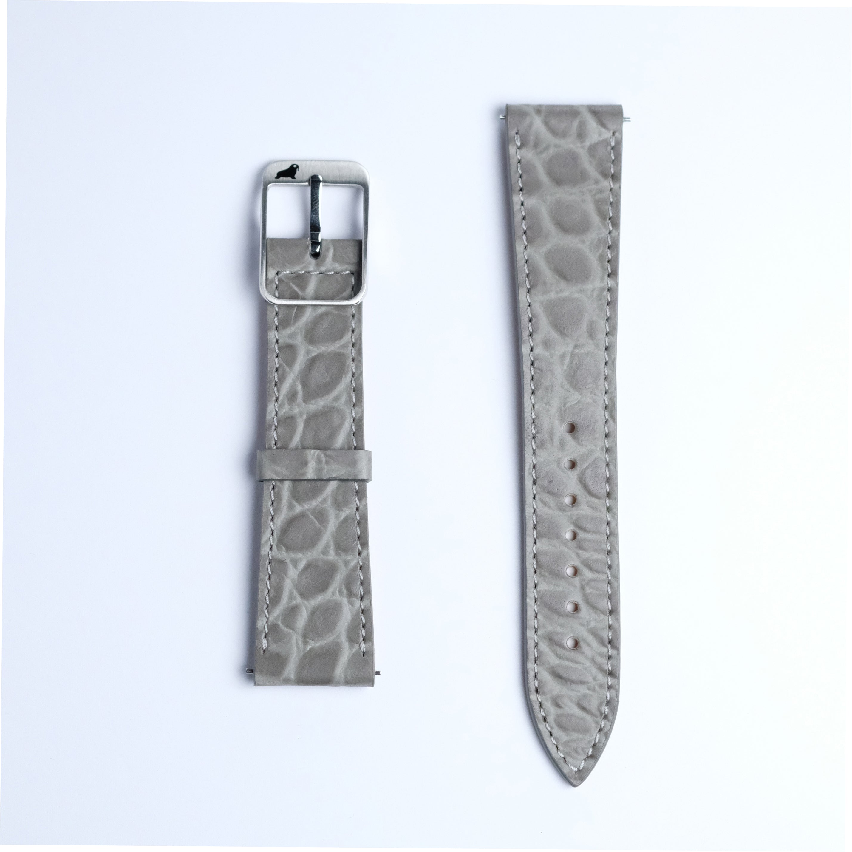 Two pieces of the RSM Watch Strap’s Alligator Circular Grain Calf Leather Watch Strap in Grey are shown side by side on a white background—one featuring a silver buckle, the other with adjustment holes.