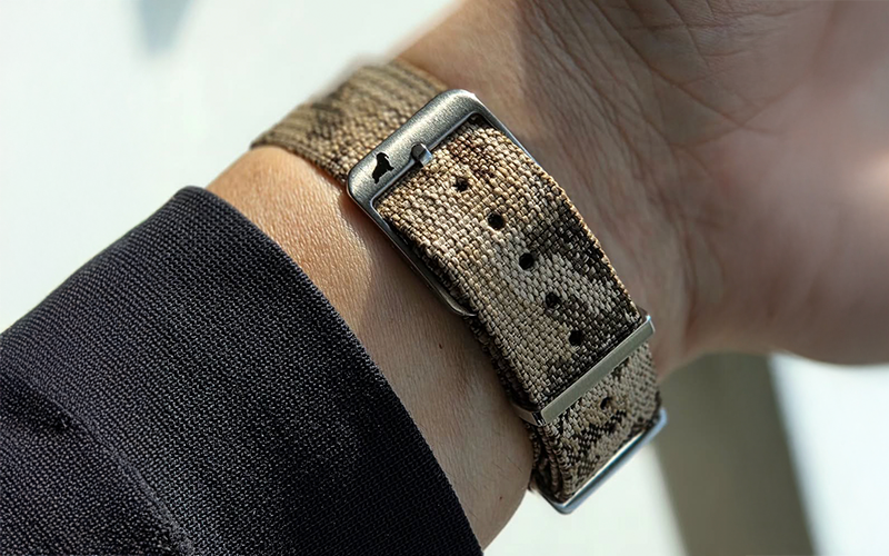 Close-up of a wrist wearing a textured camouflage watch strap with a blurred background