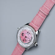The RSM Watch Strap Curved Lugs Alligator Rectangular Grain Strap in Pink is shown on a luxury wristwatch with a diamond-studded bezel and pink world time dial with city names and silver accents, set against a light gray backdrop.