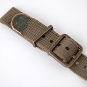 The green poly-cotton woven, vintage-style RSM watch strap features distressed bronze end caps, keeper, and a buckle with a green patina.