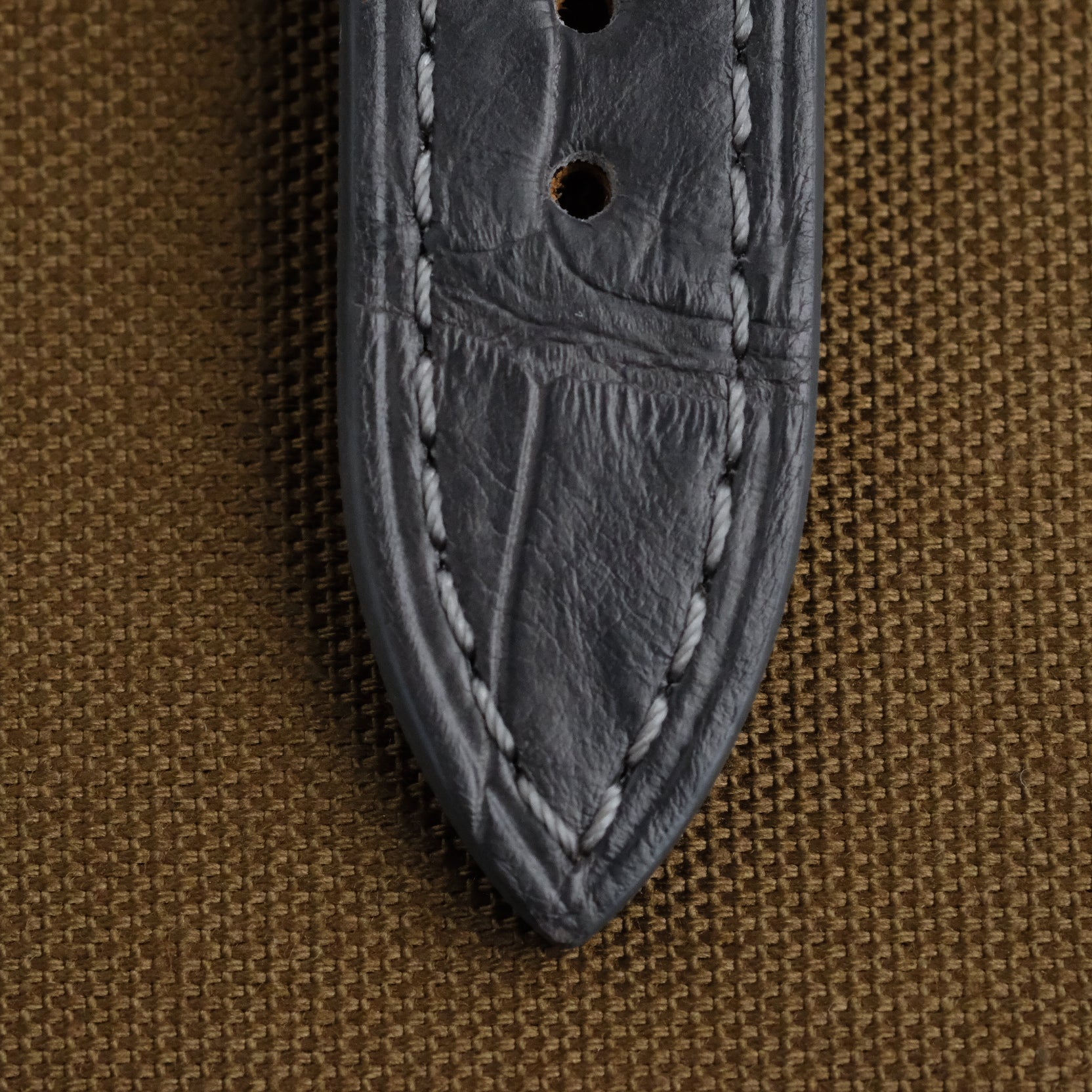 The sharp end of the grey alligator watch strap from RSM shows the clean punched holes, perfectly recessed stitches neatly in place. The soft reflection of light on the alligator leather surface shows the beauty of the complexity of the grains.