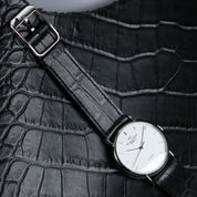 The RSM Watch Strap Curved Lugs Alligator Rectangular Grain Watch Strap in Black, paired with a white-dial wristwatch, rests on textured black leather, highlighting refined Japanese craftsmanship.