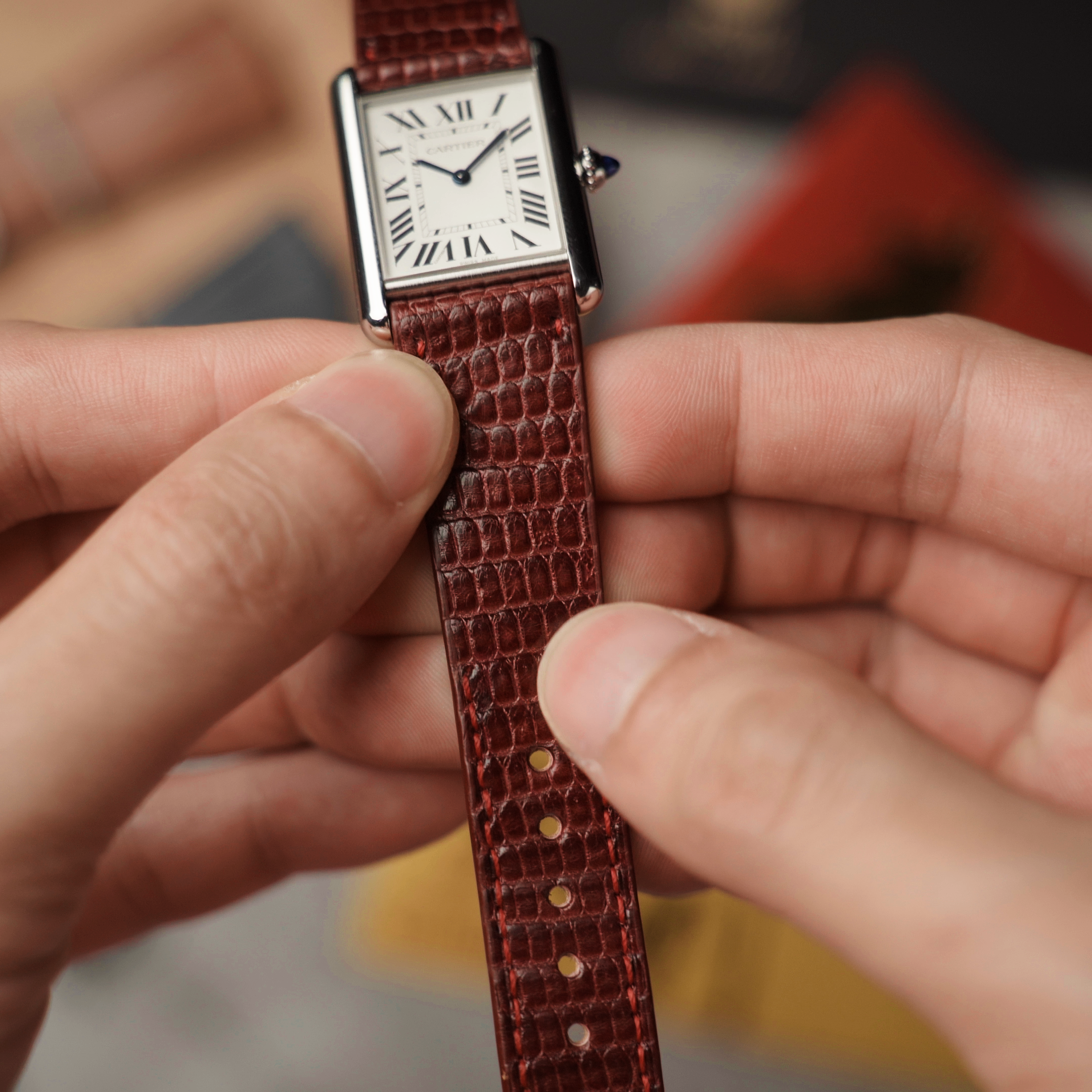 Person holding RSM's red lizard leather watch band with a blurred background