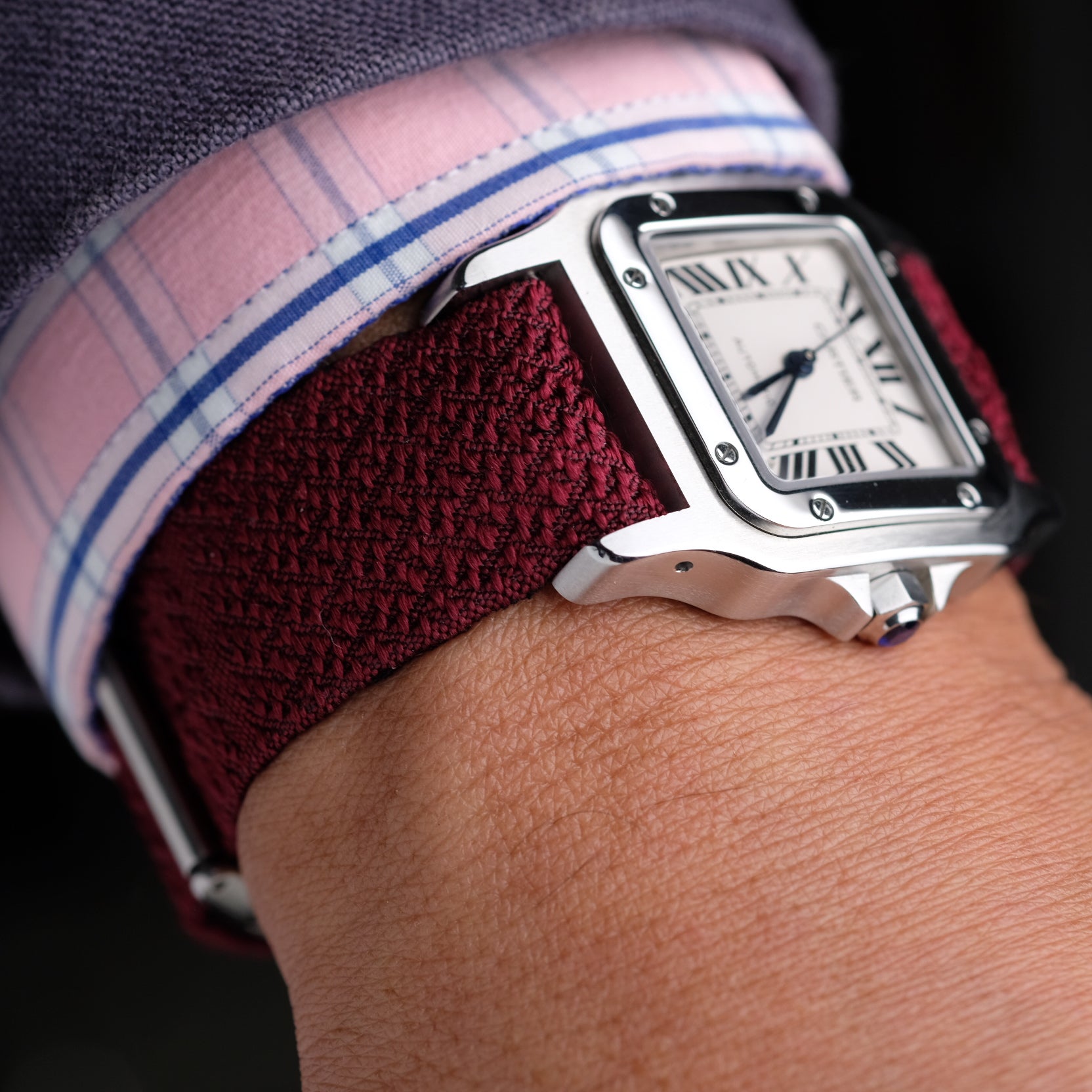 Watch with a burgundy reversible silk watch strap on a wrist, worn against a dark background