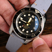 A hand adjusts the crown of a Seiko Marinemaster Professional 300m dive watch with bold markers, black dial and rotating bezel, fitted with an RSM Watch Strap Fine Canvas Strap in Metallic Blue and quick release spring bars.