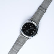 A Seiko watch with a black dial, silver markers, and date display is paired with the RSM Watch Strap Curved Lugs Alligator Rectangular Grain Watch Strap in Grey, highlighting Japanese craftsmanship on a white background.