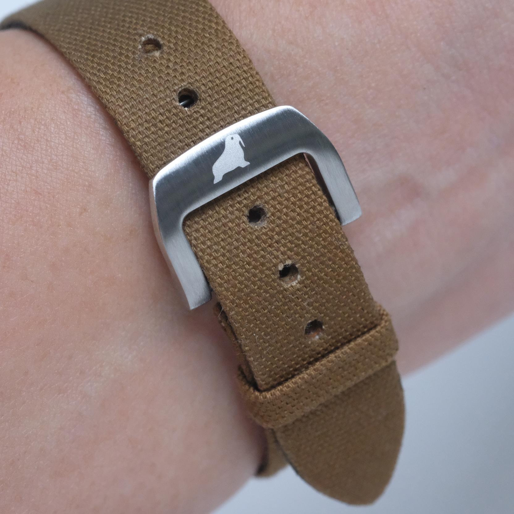RSM Walrus logo on deployant clasp with fine canvas strap on the wrist, showcasing sharp logo etching and the brushed finish of the clasp.