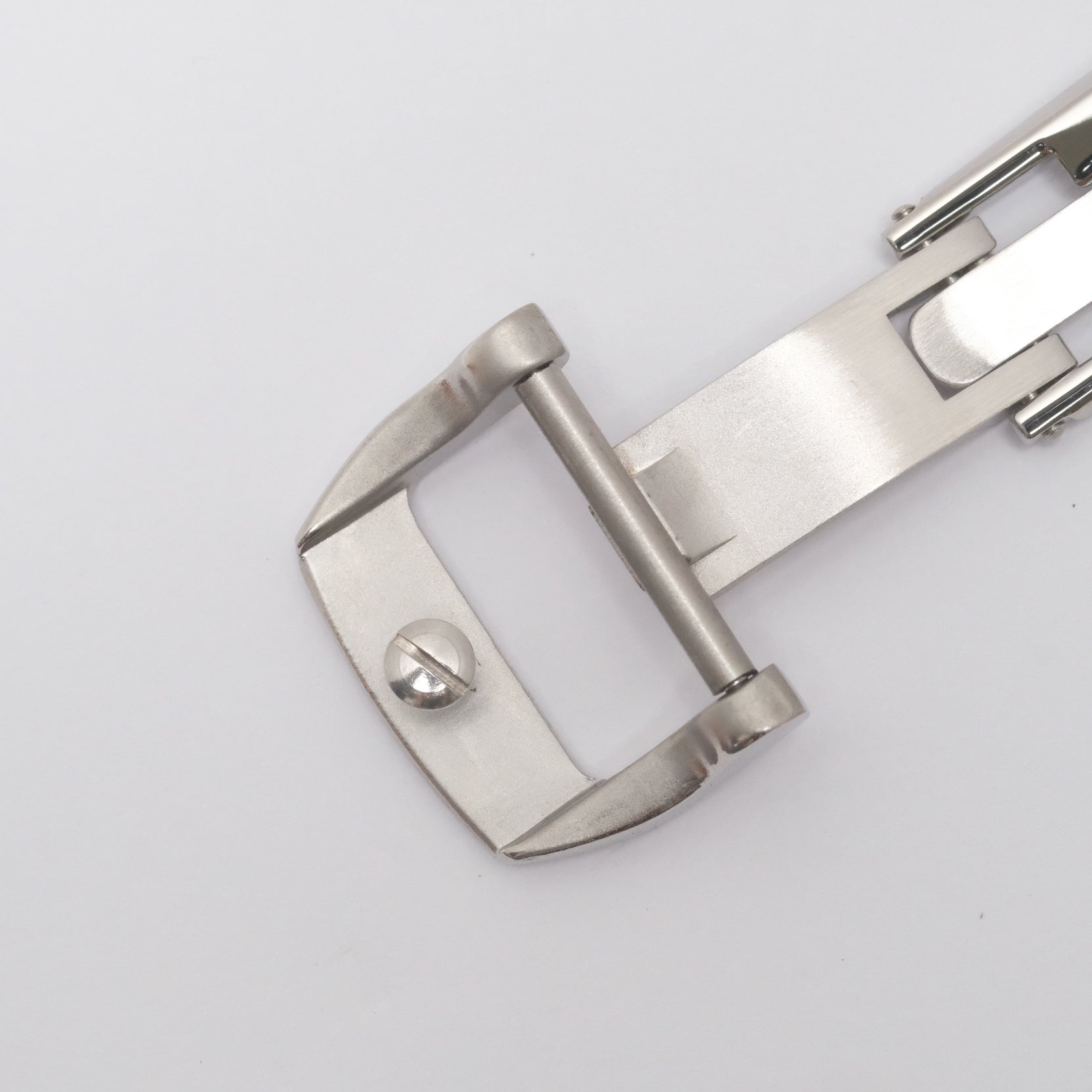 Spring-loaded steel deployant clasp buckle end showing Phillips screw cap, securing the selected strap hole in position.