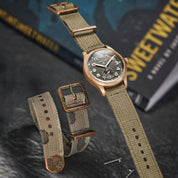 Vertex Bronze 75 watch with thick Arabic indices, fitted with RSM Vintage military green poly cotton strap, distressed bronze hardware, and green patina.