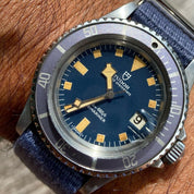 Tudor Oysterdate Submariner with a blue dial, yellow-tinted indices, and VTG Mil in Blue strap by RSM, featuring a single pass design.