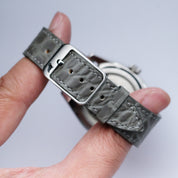 A hand holds the RSM Watch Strap Alligator Circular Grain Calf Leather Watch Strap in Grey, featuring a silver buckle and showcasing its detailed Japanese craftsmanship on the back.