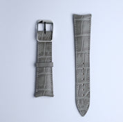 The Curved Lugs Alligator Rectangular Grain Watch Strap in Grey by RSM Watch Strap, shown in two flat pieces—one with a metal buckle and one with adjustment holes—is crafted from embossed calf leather on a white background.