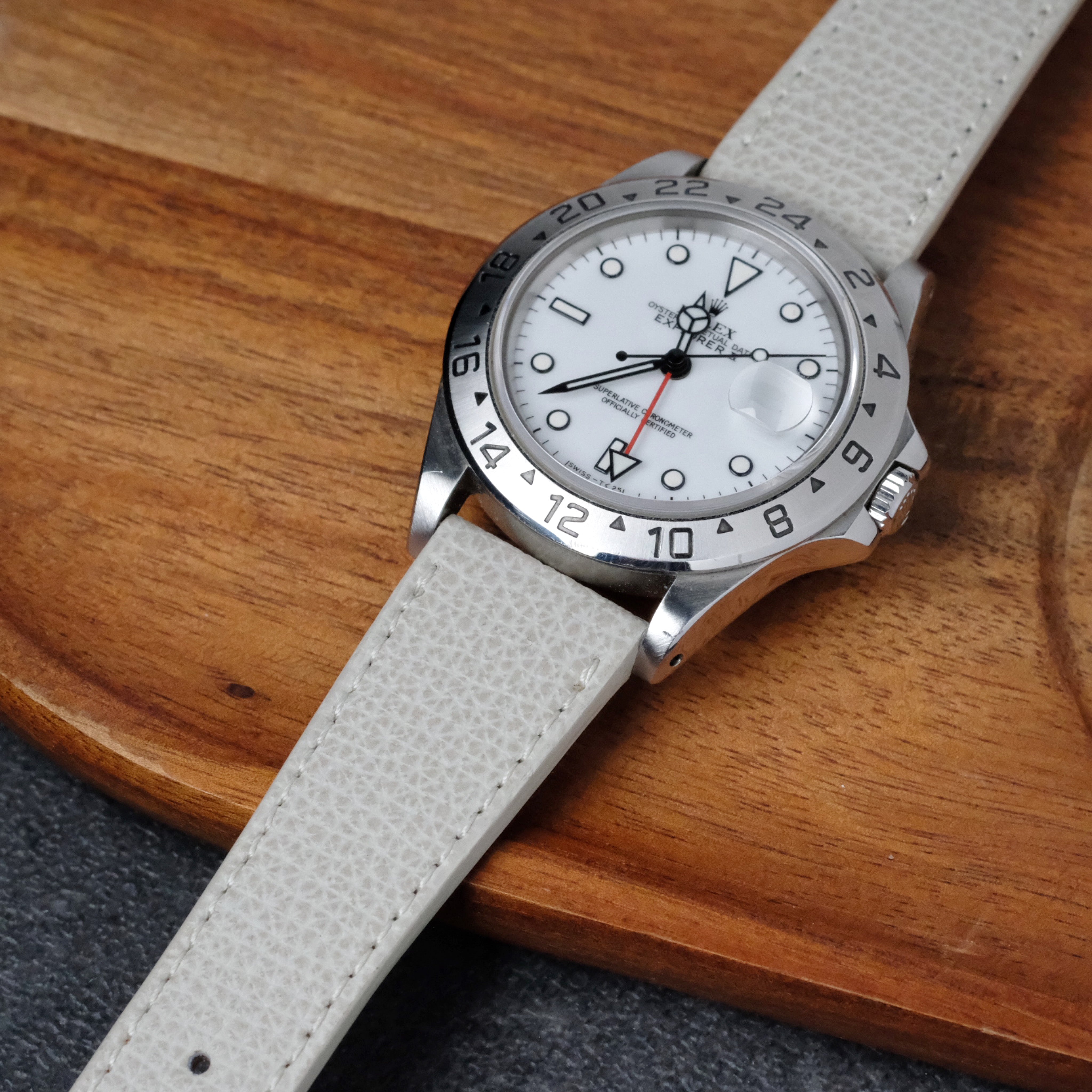 A silver Rolex watch with a white face, black hour markers, and the RSM Watch Strap Italian Epsom Leather Watch Strap in White rests on a wooden surface.