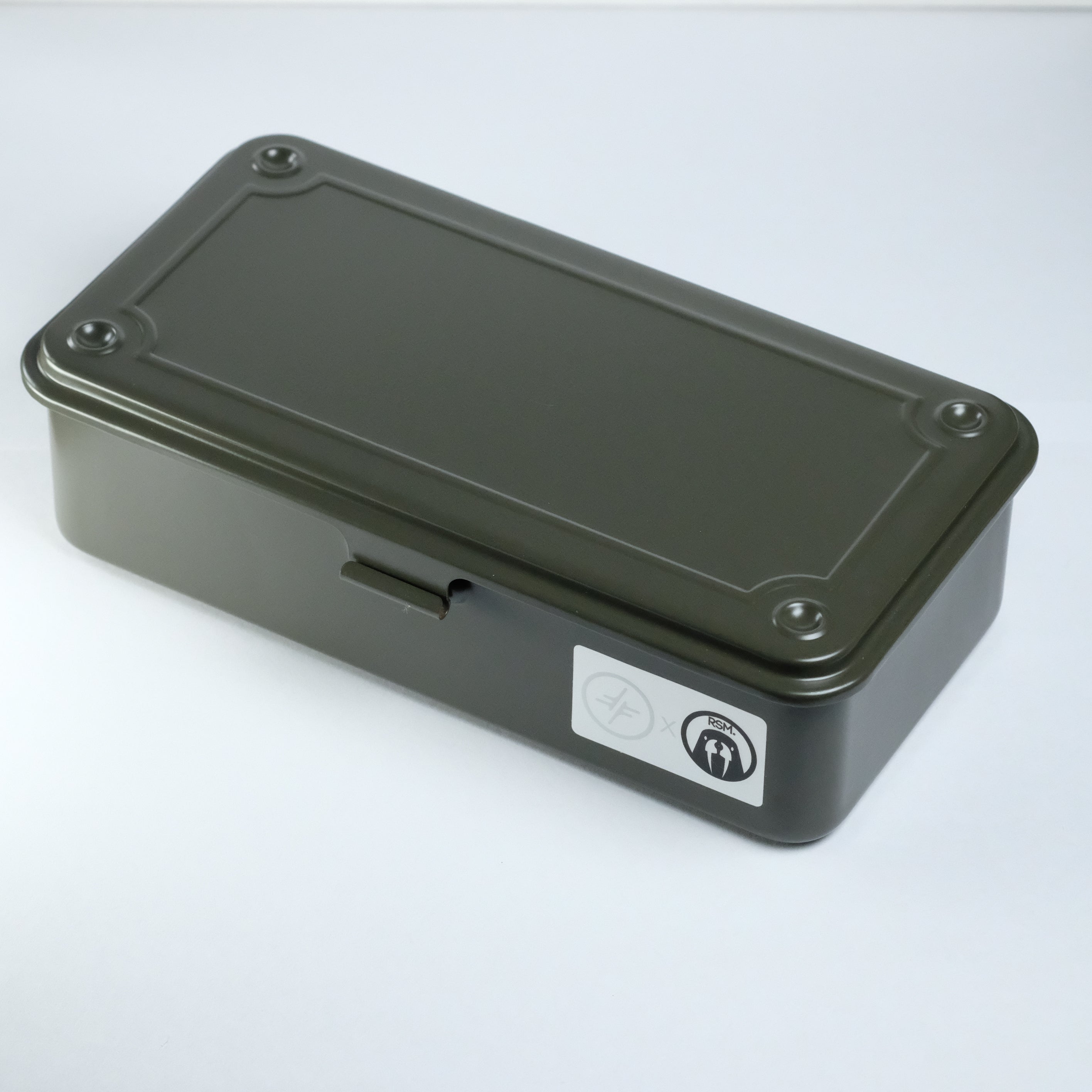 A closed, rectangular, dark green metal box with a latch on the front and a small sticker featuring icons on the side sits on a plain white surface—a perfect RSM Watch Strap Watch Tool Box T-190, ideal for watch tool or watch strap storage.
