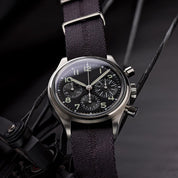 The Engraved Stripe in Stealth Gray by RSM Watch Strap features a silver chronograph with a black dial and luminous numbers on a jacquard strap.
