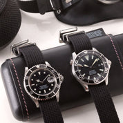 The VTG Mil in Black by RSM Watch Strap showcases two black-dial watches on NATO straps, elegantly placed on a leather watch case.